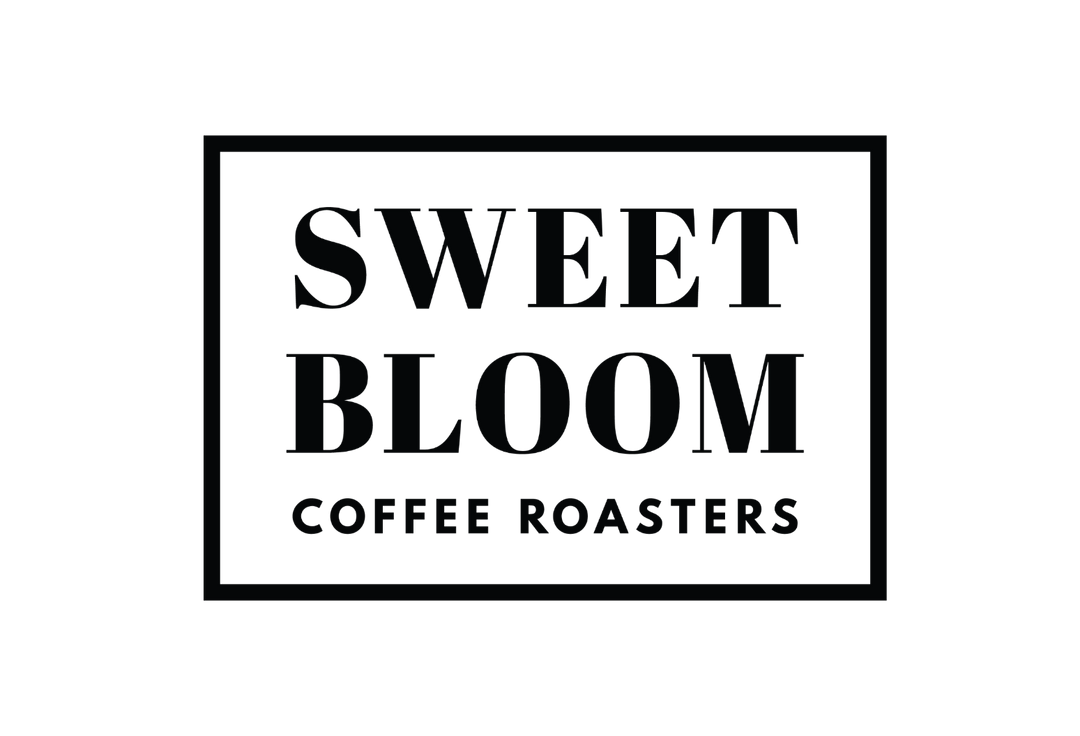 A square white sign or label with a black border, featuring the text 'SWEET BLOOM COFFEE ROASTERS' in large black serif lettering.