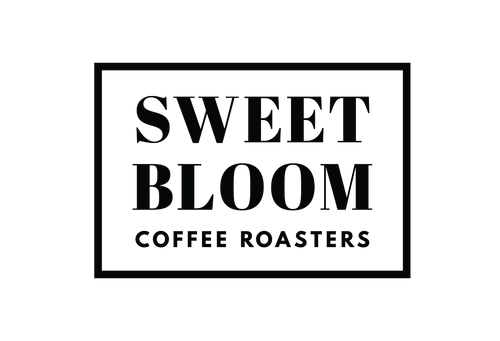A square white sign or label with a black border, featuring the text 'SWEET BLOOM COFFEE ROASTERS' in large black serif lettering.
